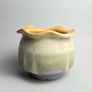 May include: A handmade ceramic plant pot with a wavy edge. The pot displays a colour gradient, shifting from a golden-yellow rim to a light green and lavender base. The pot has a rounded form and a textured surface.