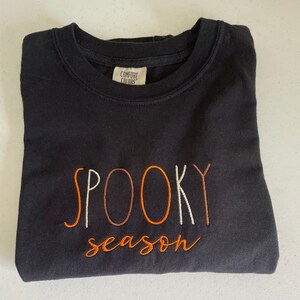 May include: Black sweatshirt with the text "SPOOKY season" embroidered in orange and white.