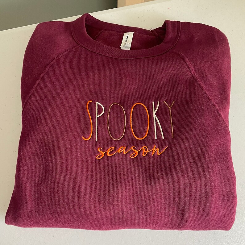 May include: Burgundy sweatshirt with the text "SPOOKY season" embroidered in white, orange, and brown thread.