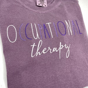May include: Purple t-shirt with the text "OCCUPATIONAL therapy" embroidered in white.