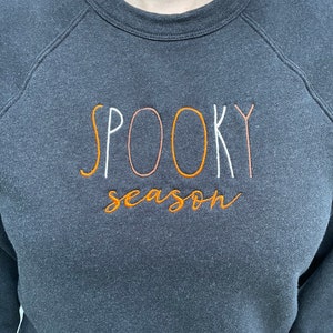 May include: A dark gray sweatshirt with the text "SPOOKY season" embroidered in orange, white, and pink.