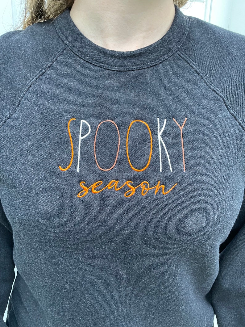 May include: A dark gray sweatshirt with the text "SPOOKY season" embroidered in orange, white, and pink.