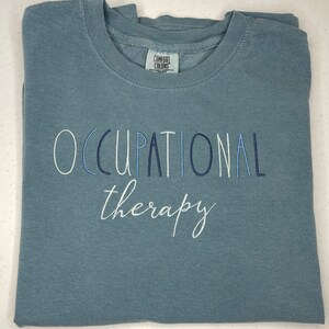May include: A light blue t-shirt with the text "OCCUPATIONAL therapy" embroidered in white and blue thread.
