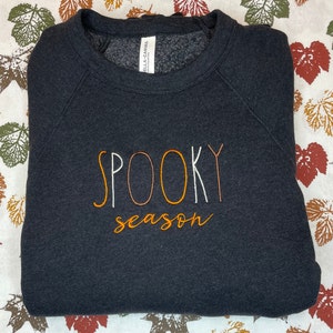 May include: Black sweatshirt with the text "SPOOKY season" embroidered in orange and white thread.