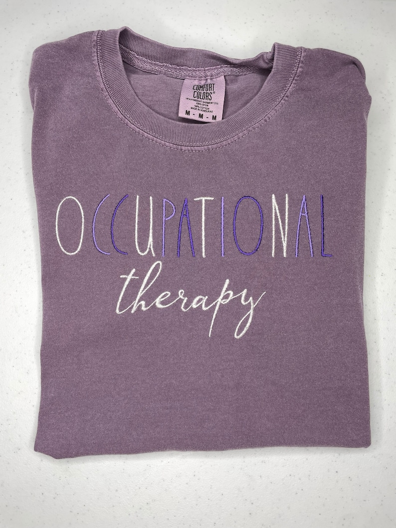 May include: A purple t-shirt with the text "Occupational therapy" embroidered in white and purple thread.