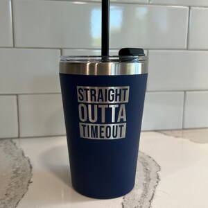 May include: A navy blue tumbler with a stainless steel lid and a black straw. The tumbler has the text "STRAIGHT OUTTA TIMEOUT" printed on it in silver.