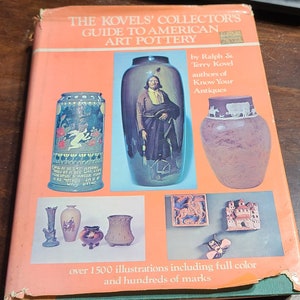 以下が含まれることがあります： 「The Kovels' Collector's Guide to American Art Pottery」という本の表紙には、ネイティブアメリカンの像が描かれた花瓶、花柄のマグカップ、荷馬車を描いたピッチャーなど、さまざまな陶器がカラフルに描かれています。本のタイトルは、明るいオレンジ色の背景に太字の黒い文字で印刷されています。表紙には、著者であるラルフとテリー・コーベルの名前と、「フルカラーで1500以上のイラストと数百のマーク」というテキストも記載されています。