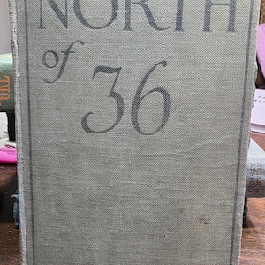 May include: A vintage book titled "North of 36" by Emerson Hough. The book has a faded green cover with the title and author's name in dark gray lettering. The book's spine is visible, and the edges show signs of wear.