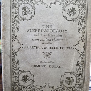 Pode incluir: Uma capa de livro antigo com o título "THE SLEEPING BEAUTY and other fairy tales FROM THE OLD FRENCH", recontado por Sir Arthur Quiller-Couch, ilustrado por Edmund Dulac. A capa é cinza com desenhos florais e querubins pretos.