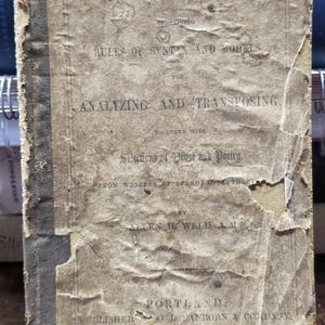 May include: An antique, weathered book titled Parsing Book, Containing Rules of Syntax and Models for Analyzing and Transposing, Together with Selections of Prose and Poetry by Allen H. Weld, A.M., published in Portland, Boston, and Philadelphia.
