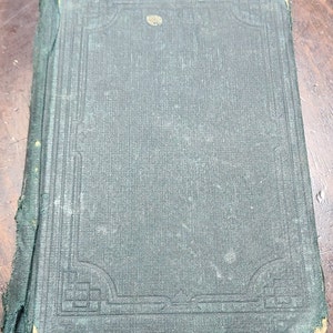 May include: A dark green hardcover book with a decorative border design on the front cover. The book is slightly worn and has a small, round, gold sticker on the front cover.
