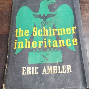 May include: A black book cover with a green eagle with a swastika on its chest. The title is "the Schirmer inheritance" in yellow letters. The author's name, "ERIC AMBLER", is in yellow letters at the bottom.