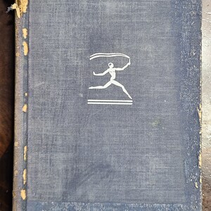 May include: A blue hardcover book with a white illustration of a person running with a ribbon on a blue background.