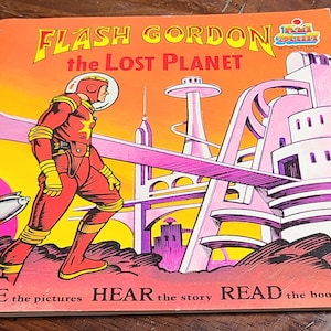 Puede incluir: Una portada de cómic vintage con Flash Gordon, un superhéroe con un traje rojo, de pie en un paisaje urbano futurista rosa y blanco. La portada dice "FLASH GORDON the LOST PLANET".