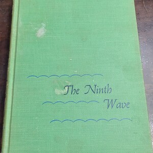 May include: A green book with the title "The Ninth Wave" printed in black cursive font. The title is surrounded by three blue wavy lines.
