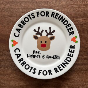 May include: White ceramic plate with the text "CARROTS FOR REINDEER" in black around the rim. A reindeer face is in the center, with the text "love, Harper & Hunter" below. Orange carrot illustrations are on the plate.