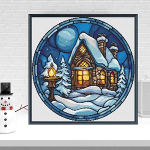 May include: A framed, circular winter scene with a snow-covered cottage, trees, and a full moon. The artwork is in a stained-glass style, with a blue and white color palette. A snowman with a top hat and a scarf is in the foreground.