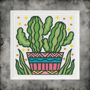 May include: A green cactus plant with multiple stems in a pink and blue patterned pot with yellow accents. The cactus is surrounded by green leaves and yellow stars.