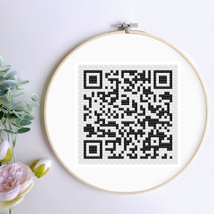 Könnte beinhalten: Ein schwarz-weißer QR-Code wird in einem runden, hölzernen Stickrahmen angezeigt. Der Rahmen befindet sich auf einem weißen Hintergrund.