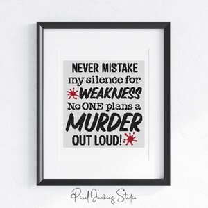 Op de afbeelding: Ingelijste kunstdruk met een zwarte lijst en een witte passe-partout. De print toont de tekst "NEVER MISTAKE my silence for WEAKNESS. No ONE plans a MURDER OUT LOUD!" in zwart en rood. Kunstwerk van Pixel Junkies Studio.
