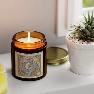 Puede incluir: Un tarro de vela de vidrio marrón con una vela blanca en su interior. El tarro tiene una etiqueta con un mapa vintage del Ártico y el texto "Mercator Arctic Map".
