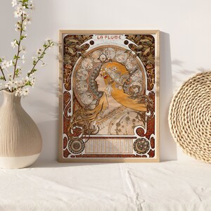 May include: A vintage poster with the title "La Plume" featuring a woman with long flowing blonde hair and a crown of flowers. The woman is surrounded by a circular design of zodiac symbols and floral motifs. The poster is framed in a wooden frame.