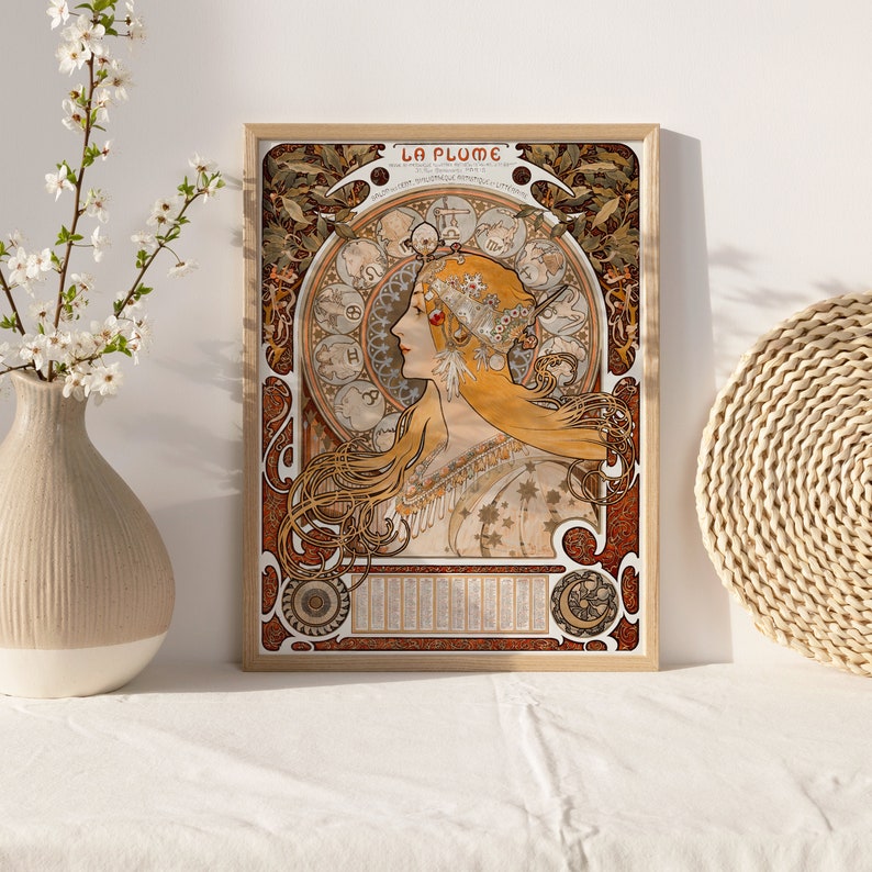 May include: A vintage poster with the title "La Plume" featuring a woman with long flowing blonde hair and a crown of flowers. The woman is surrounded by a circular design of zodiac symbols and floral motifs. The poster is framed in a wooden frame.