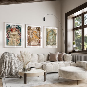 May include: Three framed art prints with a vintage aesthetic, featuring illustrations of women in ornate frames. The prints are hanging on a white wall above a white sofa with a light brown throw blanket and a white ottoman.