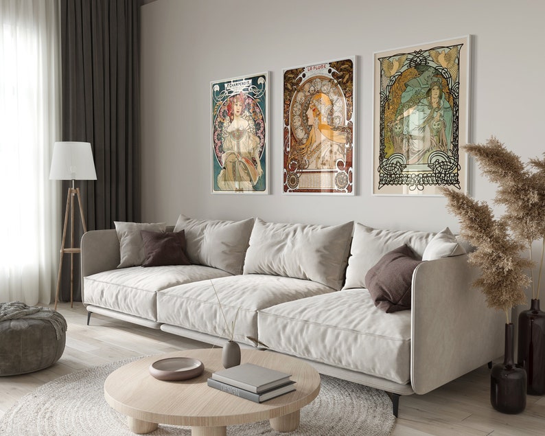 May include: Three framed art prints featuring vintage illustrations of women in ornate frames. The prints are hung on a white wall above a light-colored sofa.