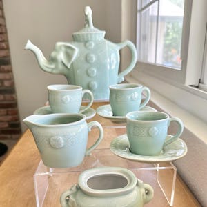 May include: A light green ceramic tea set with an elephant teapot, creamer, sugar bowl, and four cups and saucers. The set features a delicate floral design.