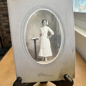 Fotografía antigua de una joven estudiante de enfermería, graduada, en blanco y negro, en un marco de cartón original, sin soporte, finales del siglo XIX y principios del XX.