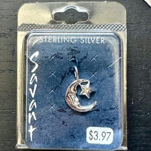 May include: A sterling silver pendant featuring a crescent moon and a star, displayed in a clear plastic package. The package has the word "Savant" printed vertically on the left side and "STERLING SILVER" at the top.