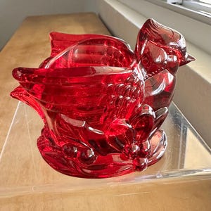 Könnte beinhalten: Eine dekorative Schale in Form eines Vogels, hergestellt aus rotem Glas. Das Design umfasst detaillierte Feder- und Blumenmuster. Der Vogel sitzt auf einem Sockel mit weiteren Details, was ihn zu einem auffälligen Dekorationsartikel macht.