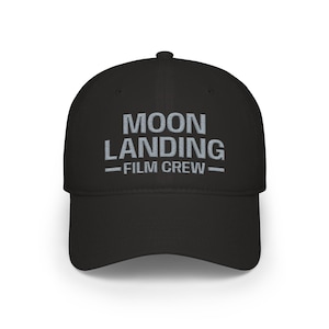 May include: Black baseball cap with the text "MOON LANDING - FILM CREW" in gray lettering. The cap has a curved brim and a structured crown. A stylish accessory for film enthusiasts.
