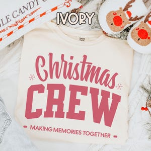 May include: Ivory Christmas Crew t-shirt with red text. The shirt displays "Christmas CREW" in a bold font, with "MAKING MEMORIES TOGETHER" underneath. A festive holiday theme.