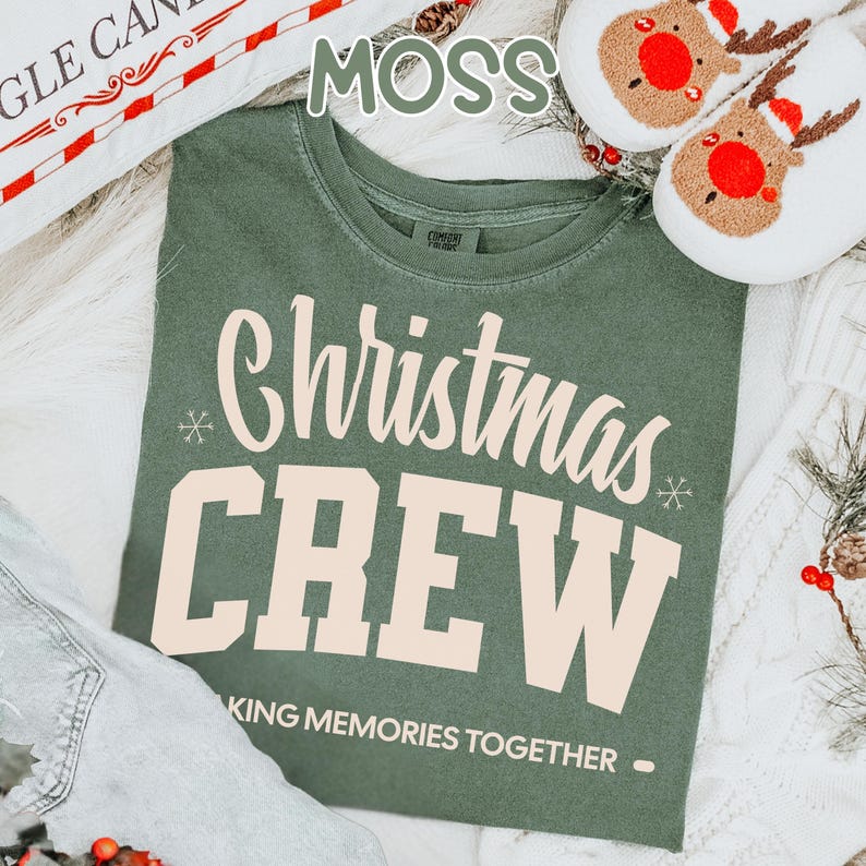 May include: A moss green t-shirt with the words "Christmas CREW" in cream. The text "MAKING MEMORIES TOGETHER" is below. The image also shows reindeer slippers and a decorative pillow.