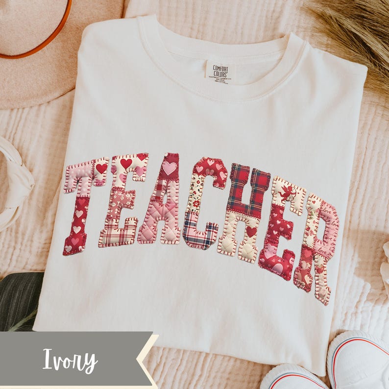 May include: Ivory t-shirt featuring the word "TEACHER" appliqu&eacute;d across the front. The letters are crafted from diverse red and pink patterned fabrics, including hearts and plaid. The shirt is a Comfort Colors brand.