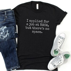 May include: Black t-shirt with white text that reads "I applied for a job at NASA, but there's no space."