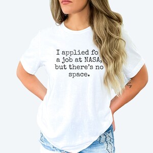 May include: White t-shirt with a black text graphic that reads "I applied for a job at NASA, but there's no space."