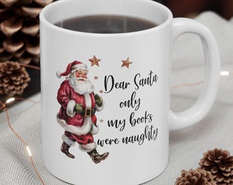 May include: White ceramic mug with a handle, featuring a Santa Claus illustration in a red suit with white trim. The mug has the text "Dear Santa only my books were naughty" and three star accents.