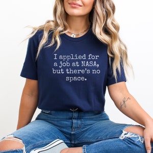 May include: A navy blue t-shirt with the text "I applied for a job at NASA, but there's no space." printed in white.