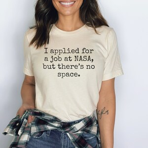 May include: A white t-shirt with the text "I applied for a job at NASA, but there's no space." printed in black.