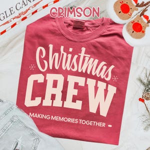 May include: Crimson red t-shirt with the words "Christmas CREW" in white block letters. The phrase "MAKING MEMORIES TOGETHER" is printed below. The shirt is displayed with reindeer slippers and festive decorations.