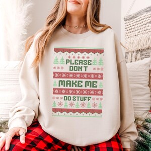 May include: A cream-colored sweatshirt with a red and green Christmas-themed design. The design features the text "Please Don't Make Me Do Stuff".