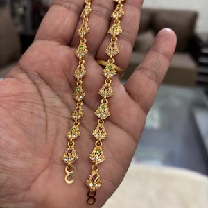 May include: A pair of gold-tone dangle earrings with a teardrop design. The earrings are adorned with small, colorful gemstones.