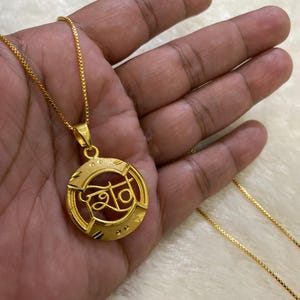 May include: A gold chain necklace with a round pendant featuring the word "श्री" in a decorative font.