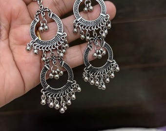 May include: Silver dangle earrings with two circular hoops and multiple small beads hanging from each hoop.