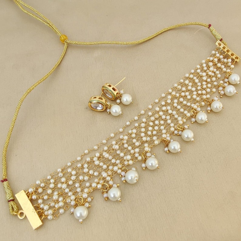 May include: A gold necklace with a layered design of white pearls and a matching pair of pearl earrings. The necklace has a gold clasp and a gold chain.