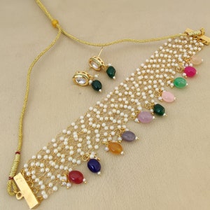 May include: A gold necklace with a multi-strand design featuring small white pearls and colorful gemstone accents. The necklace has a clasp closure and comes with matching earrings.