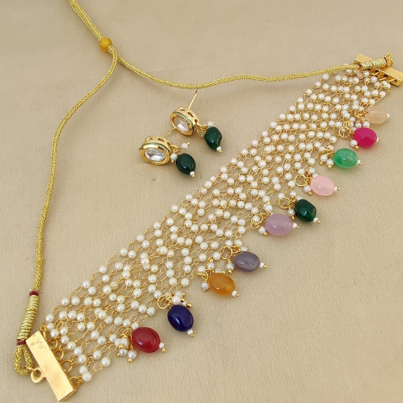 May include: A gold necklace with a multi-strand design featuring small white pearls and colorful gemstone accents. The necklace has a clasp closure and comes with matching earrings.